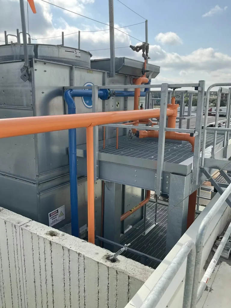 Industrial rooftop mechanical area with painted piping, safety railings, and metal platform walkways.
