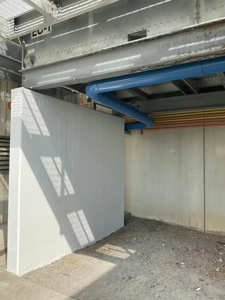 Freshly painted concrete enclosure beneath industrial equipment with exposed ductwork and color-coded piping.