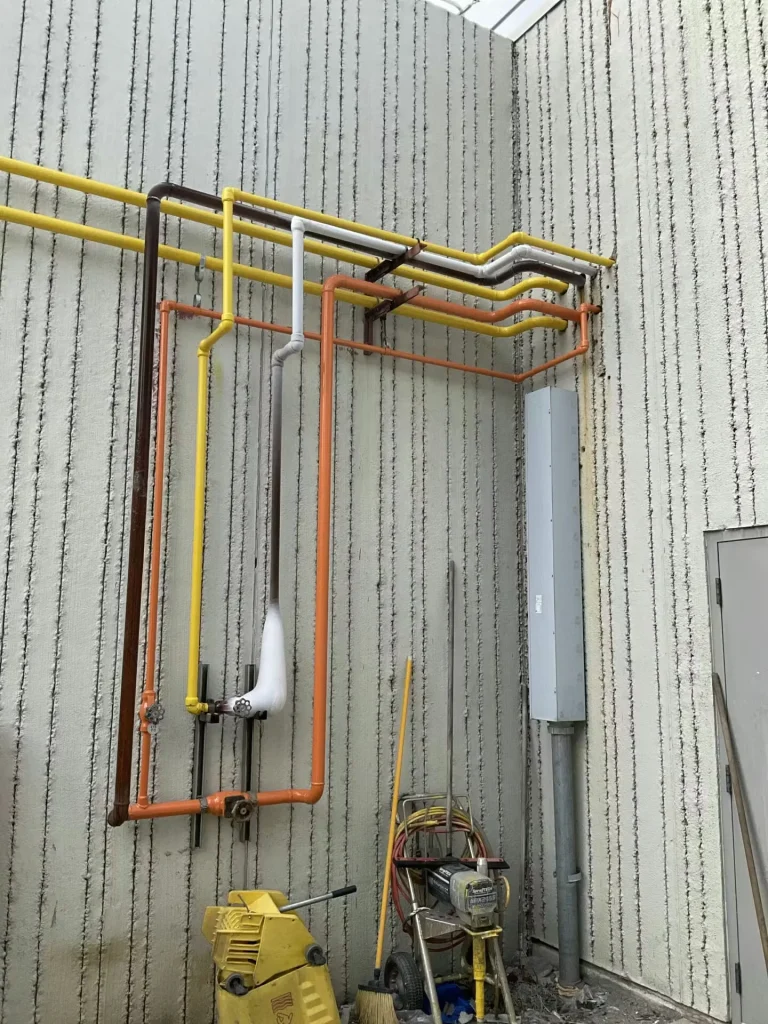 Color-coded industrial piping system mounted on textured exterior wall after facility repaint and maintenance work.