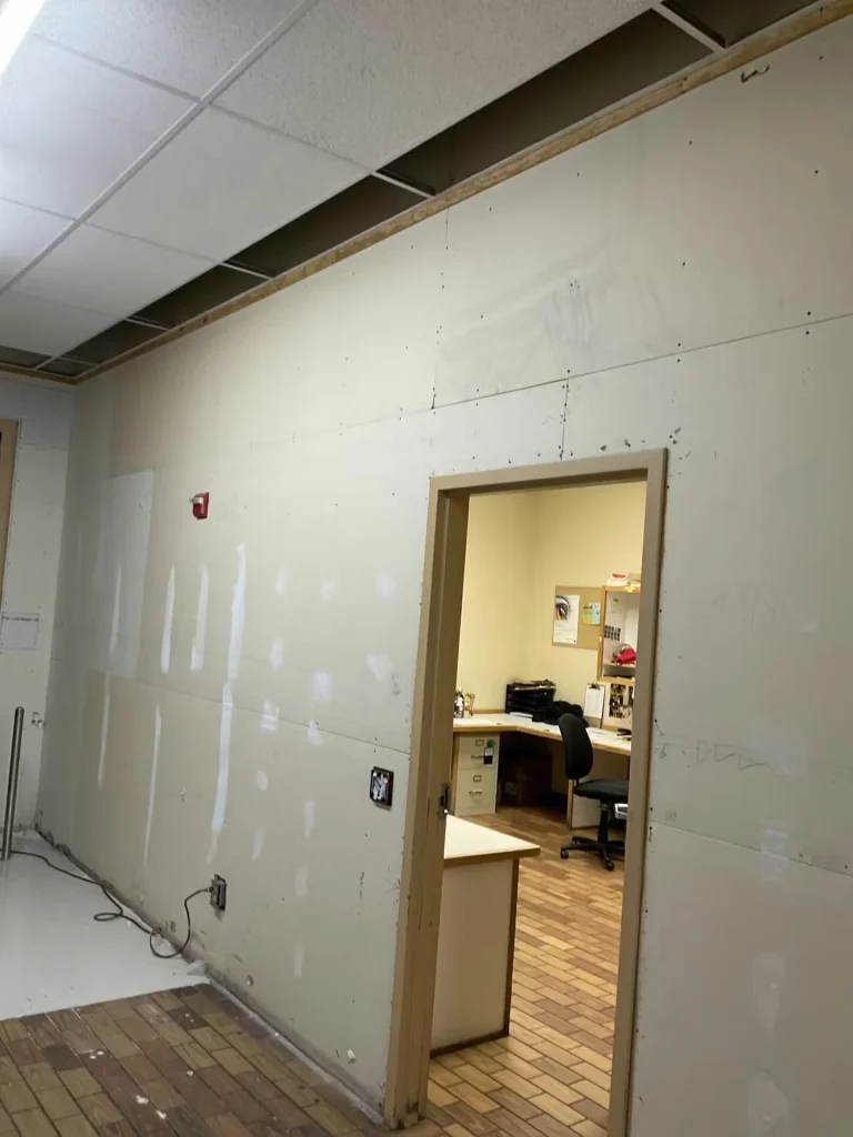 Interior commercial renovation showing unfinished drywall wall and open office doorway inside retail space