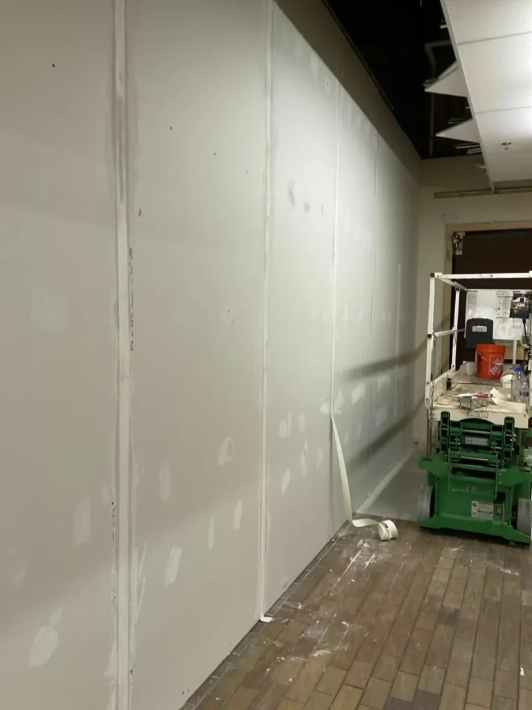 Long drywall partition wall under construction in grocery store with lift equipment and exposed ceiling above