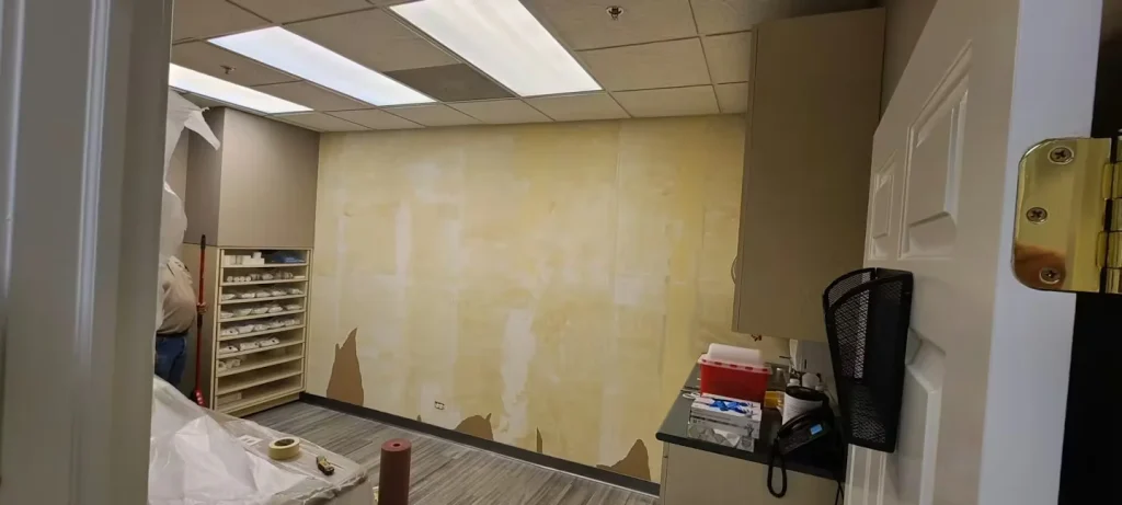 Medical office room during renovation showing wall preparation, patched surfaces, and flooring protection.