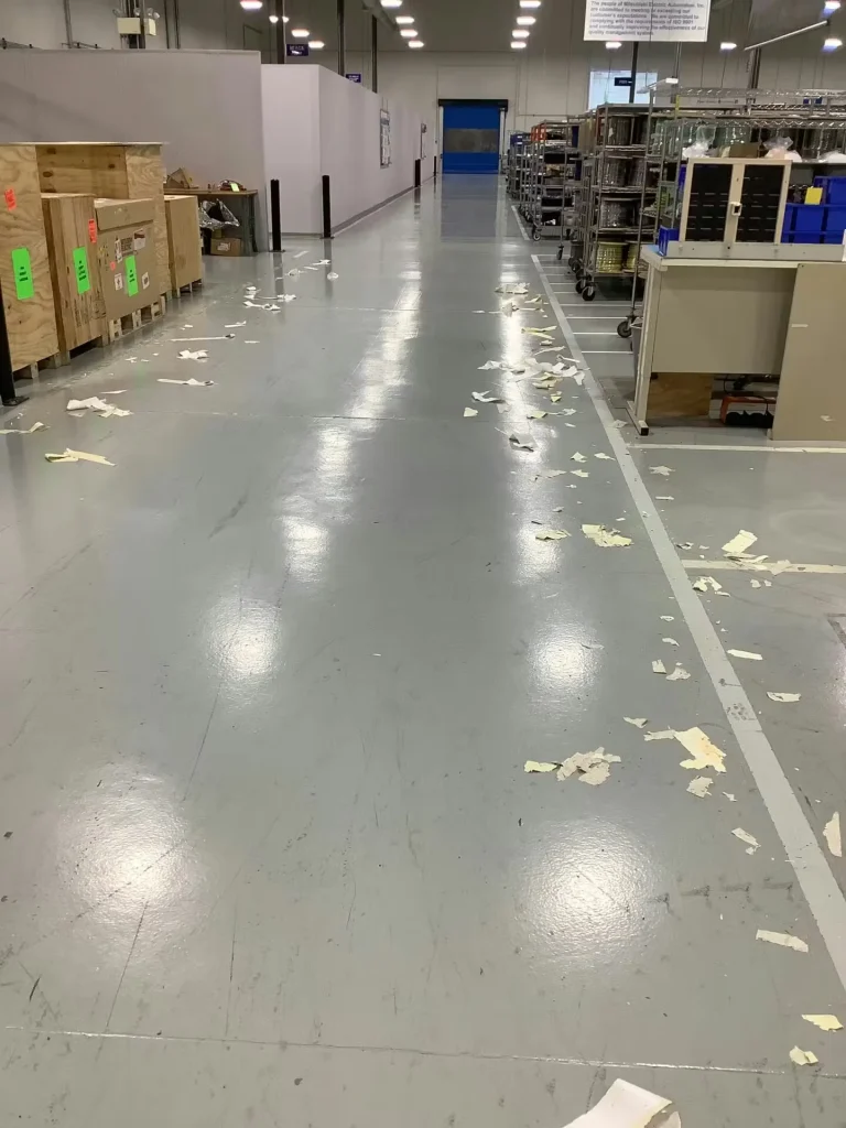 Manufacturing aisle with worn gray floor surface and debris prior to ESD floor coating application.