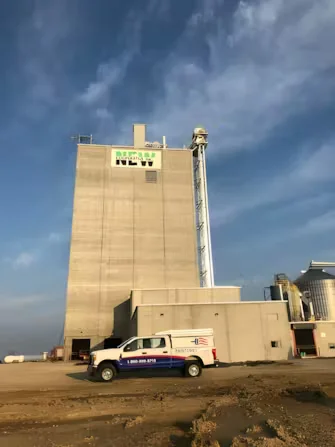 Feed mill facility with multi-story concrete structure, newly painted company logo, and service vehicle parked outside.