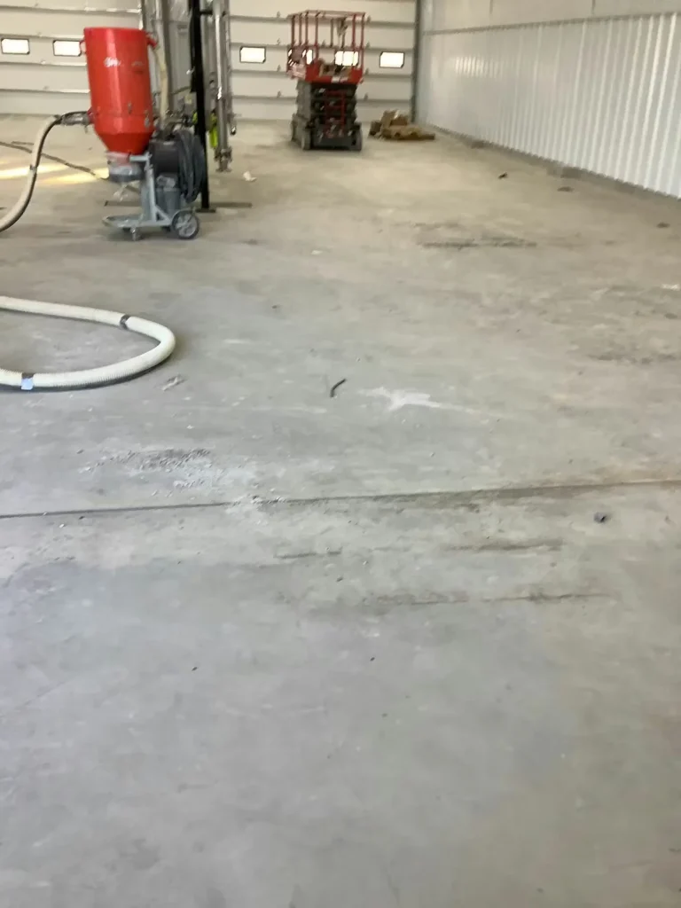 Industrial workspace during floor preparation with concrete surface, dust collection equipment, and scissor lift.