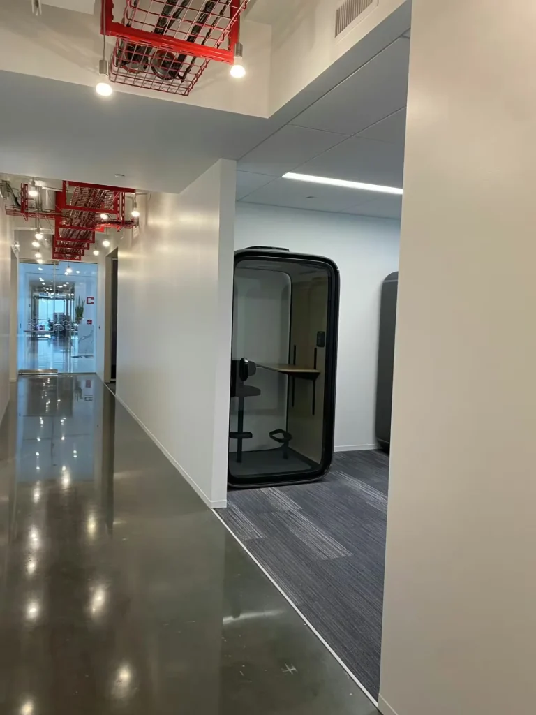 Modern office hallway with newly painted walls, glass meeting pods, exposed ceiling, and polished concrete flooring.