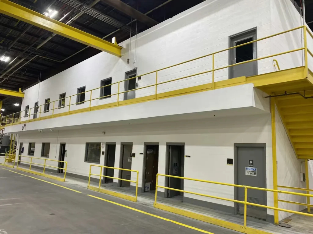 Industrial facility interior with freshly painted white walls, yellow safety railings, and second-floor office entrances