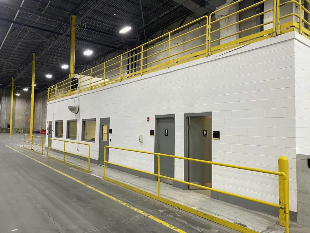 Wide interior view of an industrial warehouse with freshly painted walls, yellow overhead beams, and polished concrete floors