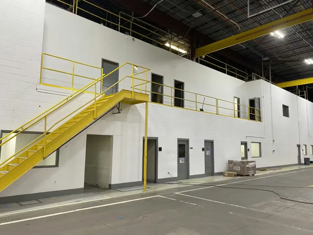 Large manufacturing floor with yellow steel columns, overhead lighting, and newly painted industrial surfaces