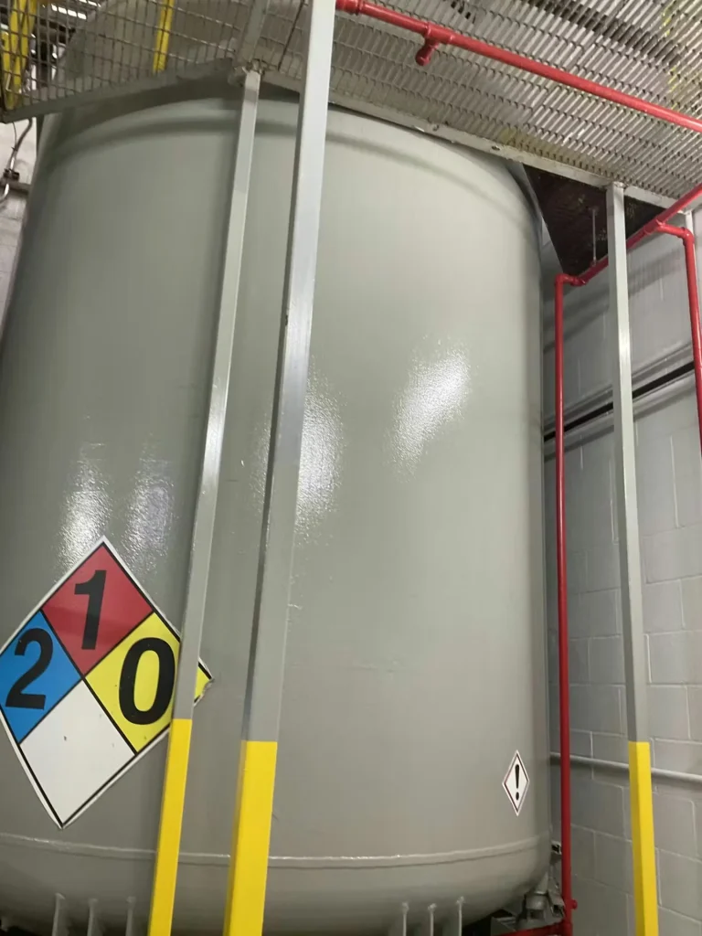 Large industrial chemical storage tank with safety placards and protective steel framing