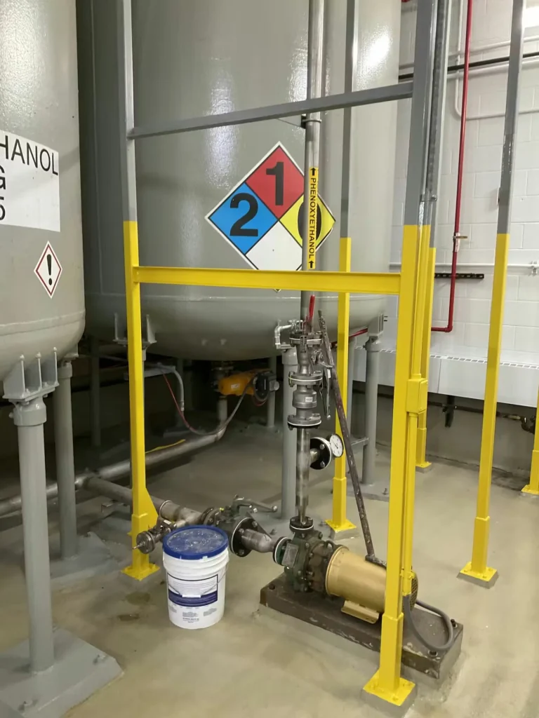 Chemical tank base with pump, valves, and yellow safety railings in pump room