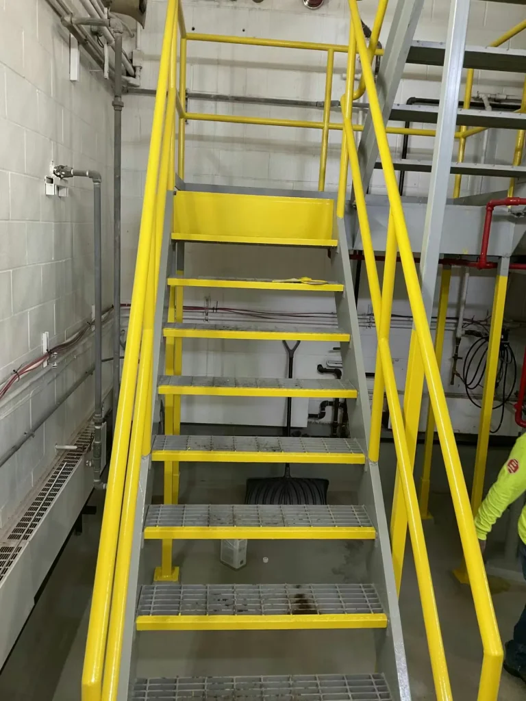 Yellow industrial metal staircase with safety railings inside mechanical room