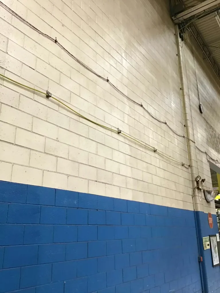 Industrial facility interior with scissor lift and newly painted blue and white masonry wall along a marked safety walkway.