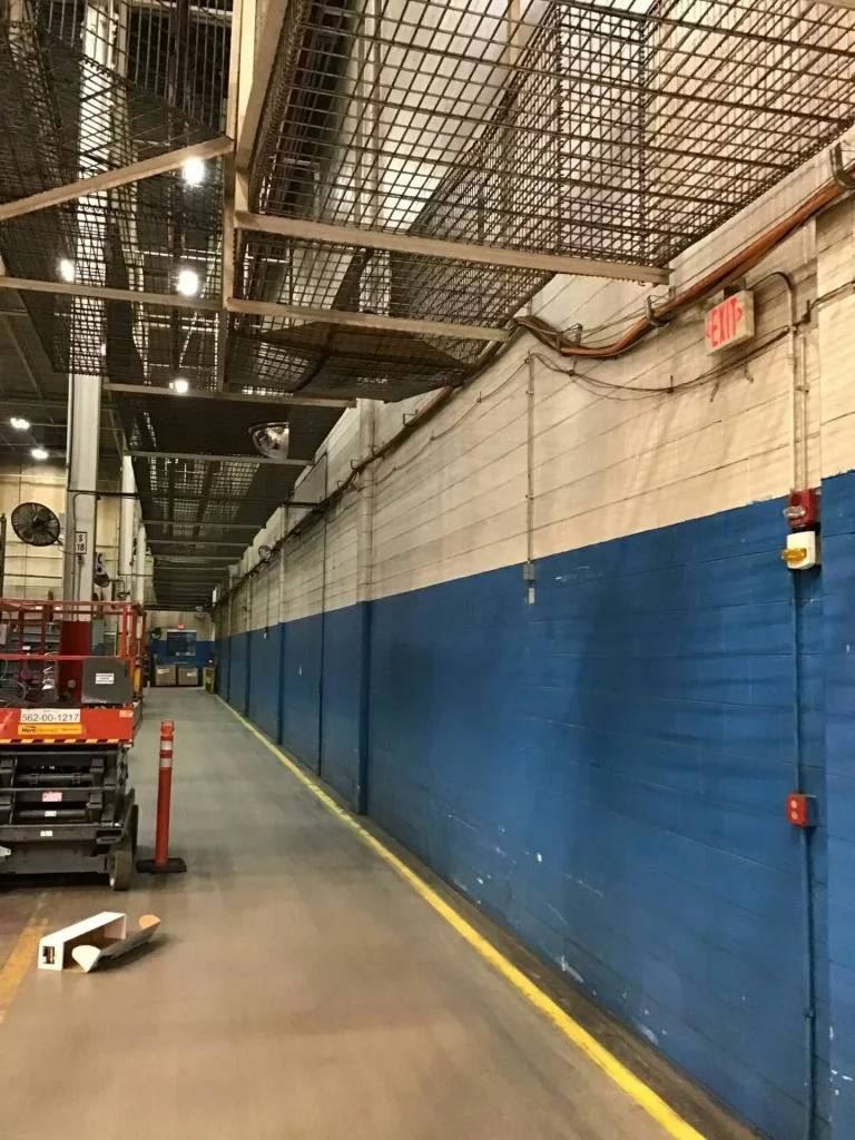 Freshly repainted industrial masonry wall with blue lower section and white upper section, featuring exposed conduit and piping.