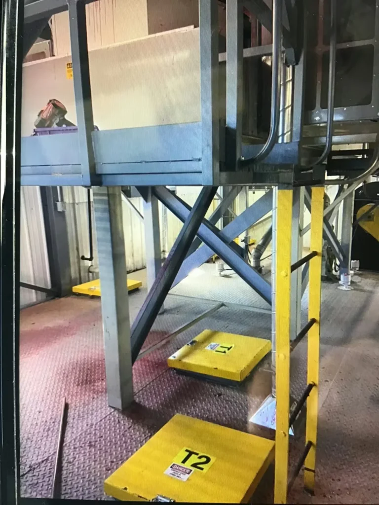 Industrial interior with steel supports, ladders, and yellow access panels on a metal floor