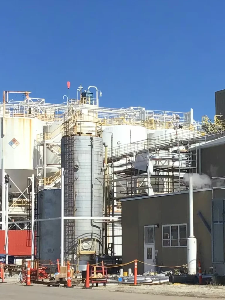 Industrial processing facility with tanks, piping, and elevated platforms under a clear blue sky