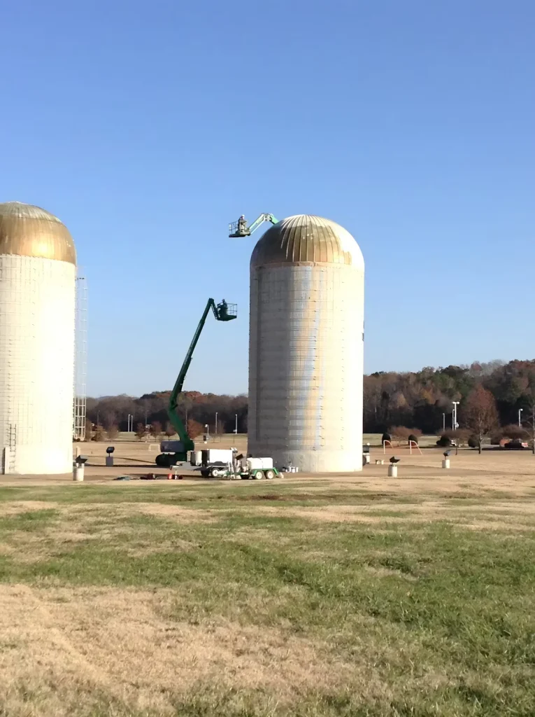 Industrial silo roof painting project using aerial lifts to apply protective coatings on concrete silos
