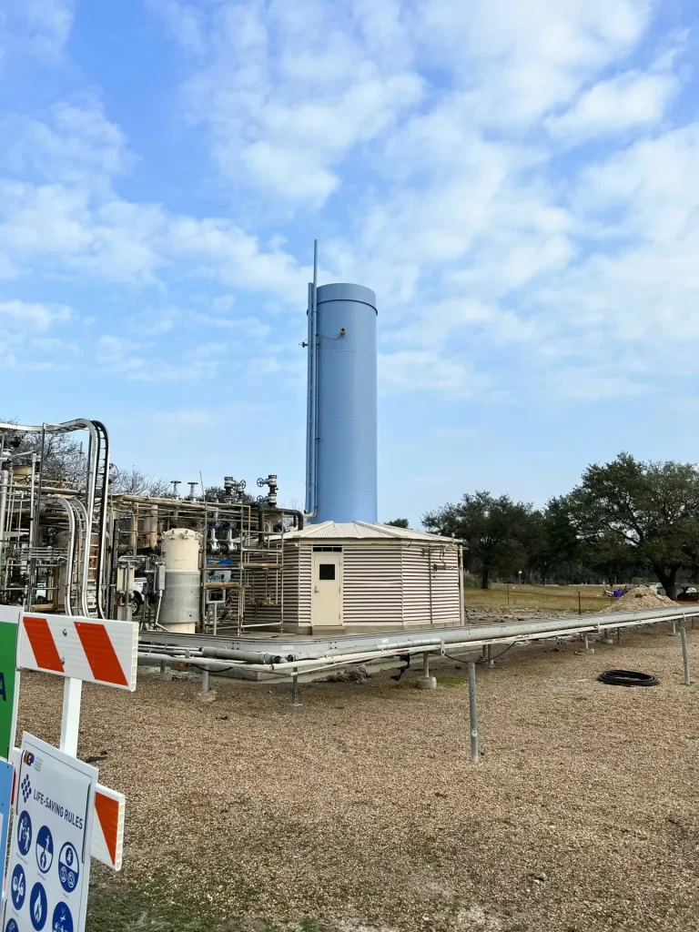 Blue industrial exhaust stack at Shell technology center with piping and safety signage in foreground