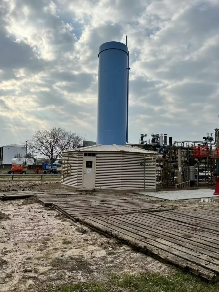 Newly coated blue vertical process stack at Shell facility under cloudy sky