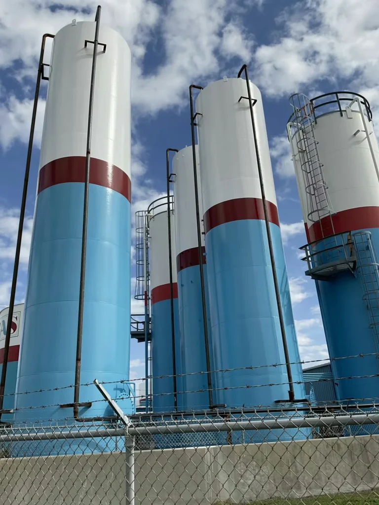 Close-up view of tall cylindrical industrial tanks with fresh white and blue paint and access ladders at an industrial facility