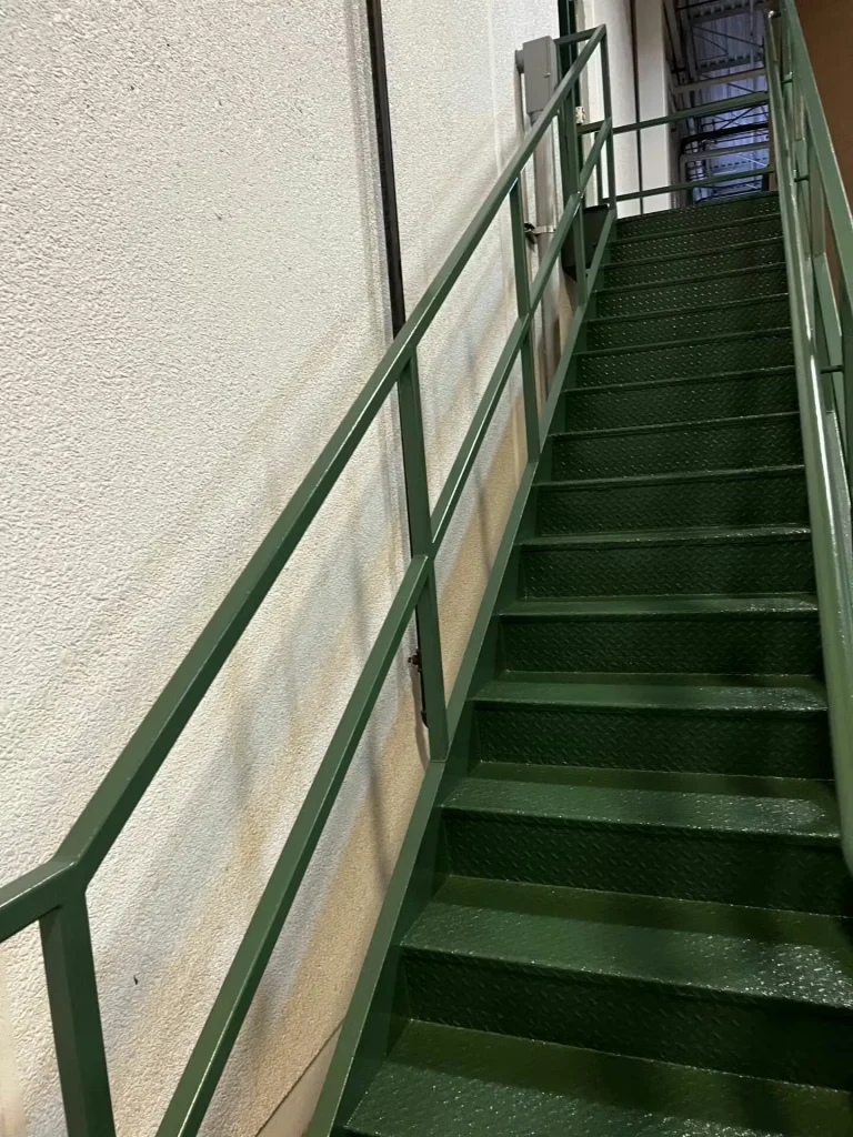 Newly coated green epoxy metal staircase with safety handrails inside industrial facility