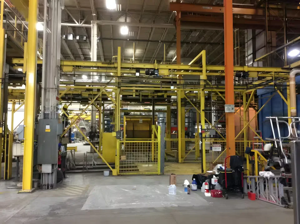 Industrial facility interior with large yellow-painted structural steel framework and heavy equipment during structural steel painting project