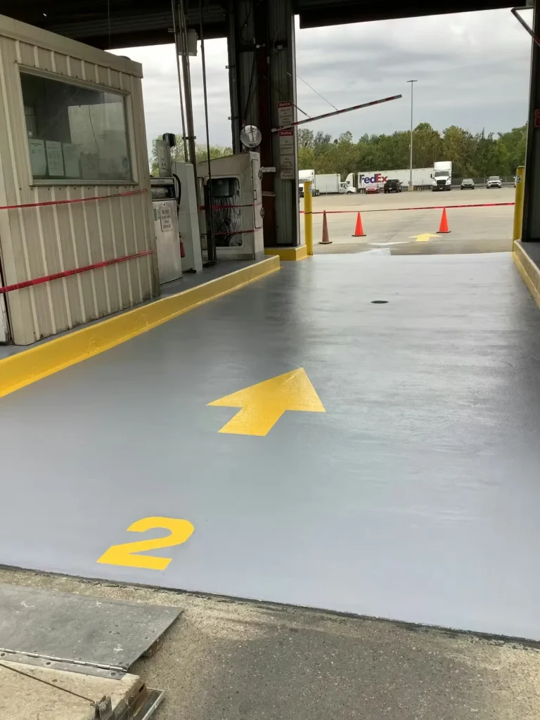 Rejuvenated concrete floor at a distribution center entry lane with yellow directional arrow, numbered marking, and safety striping leading to a truck yard