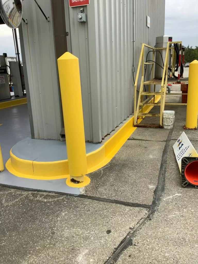 Yellow safety bollards and curb coating protecting an industrial building corner with stairs and equipment access