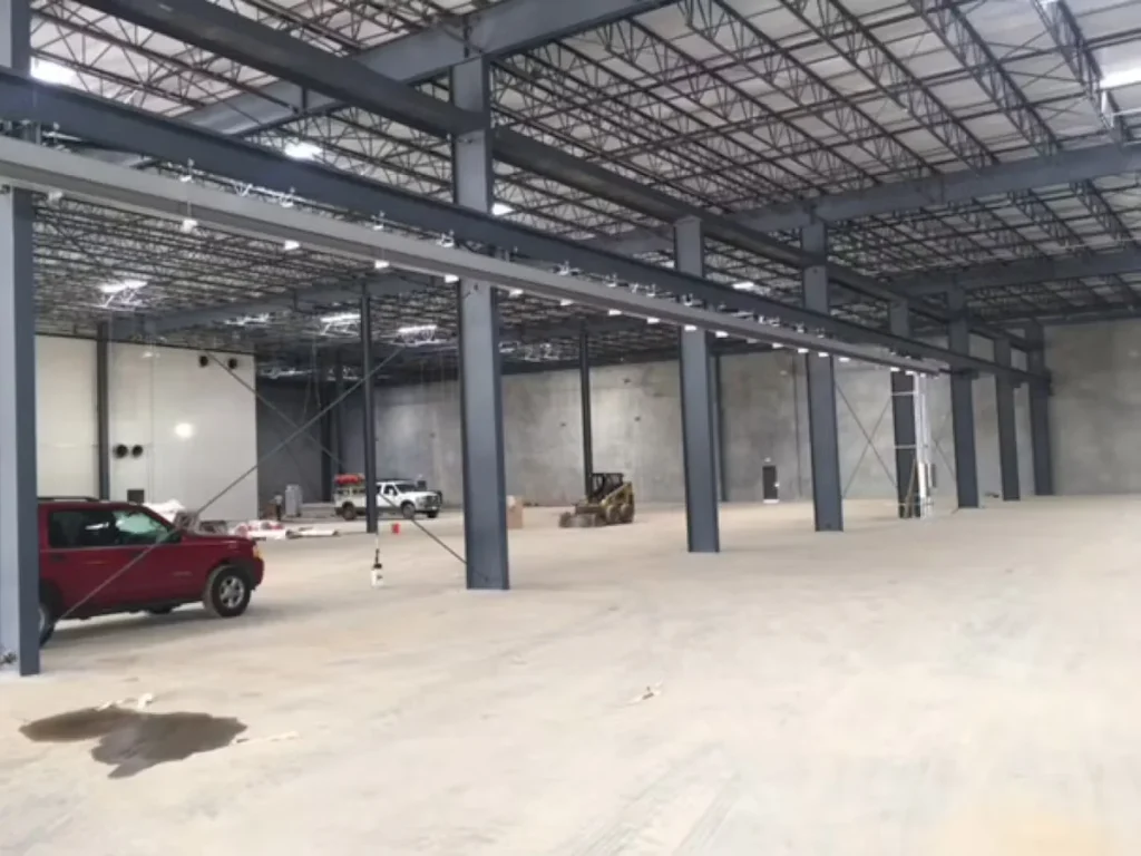 Large warehouse interior with freshly painted steel columns, open concrete floor, and construction equipment during facility painting project
