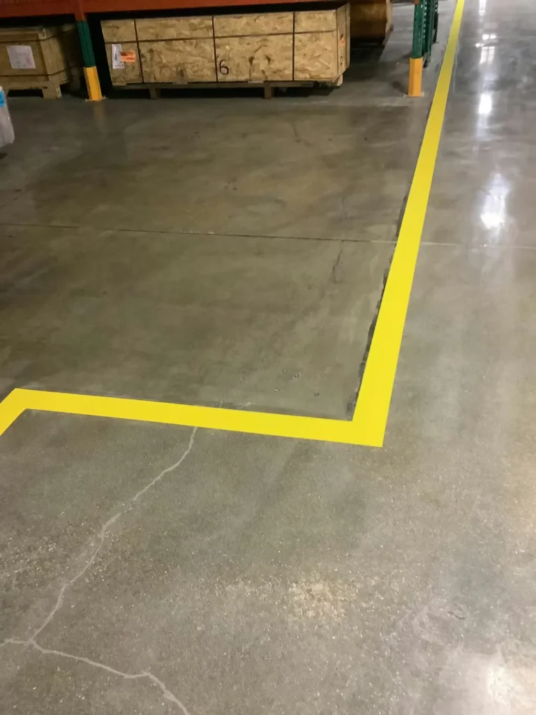 Polished concrete warehouse floor with bright yellow safety corner markings outlining a designated storage area