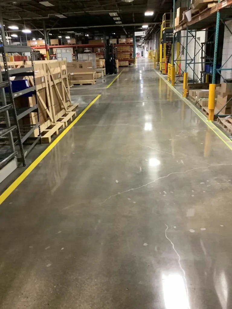 Wide warehouse aisle with polished concrete flooring, yellow safety lines, pallet racking, and stored materials along both sides