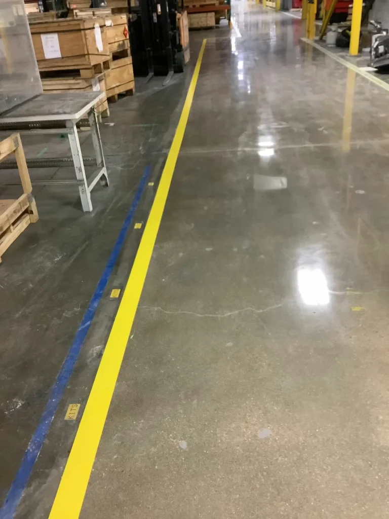 Close view of polished warehouse floor with yellow and blue line striping marking traffic lanes and work zones