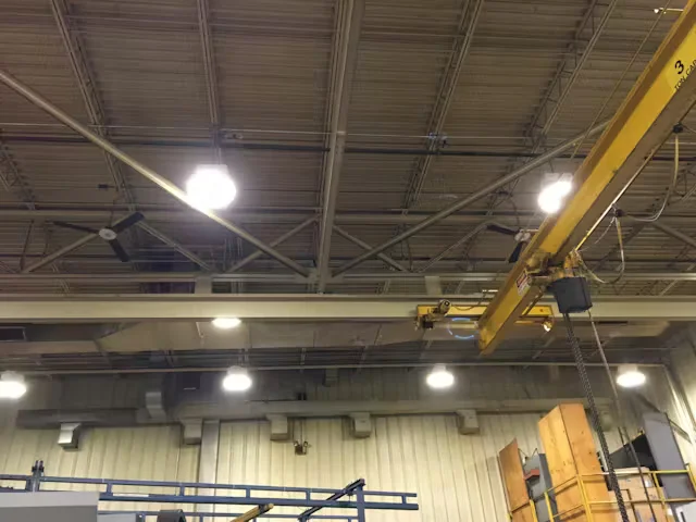 Warehouse interior ceiling with exposed steel beams, overhead lights, and yellow overhead crane system