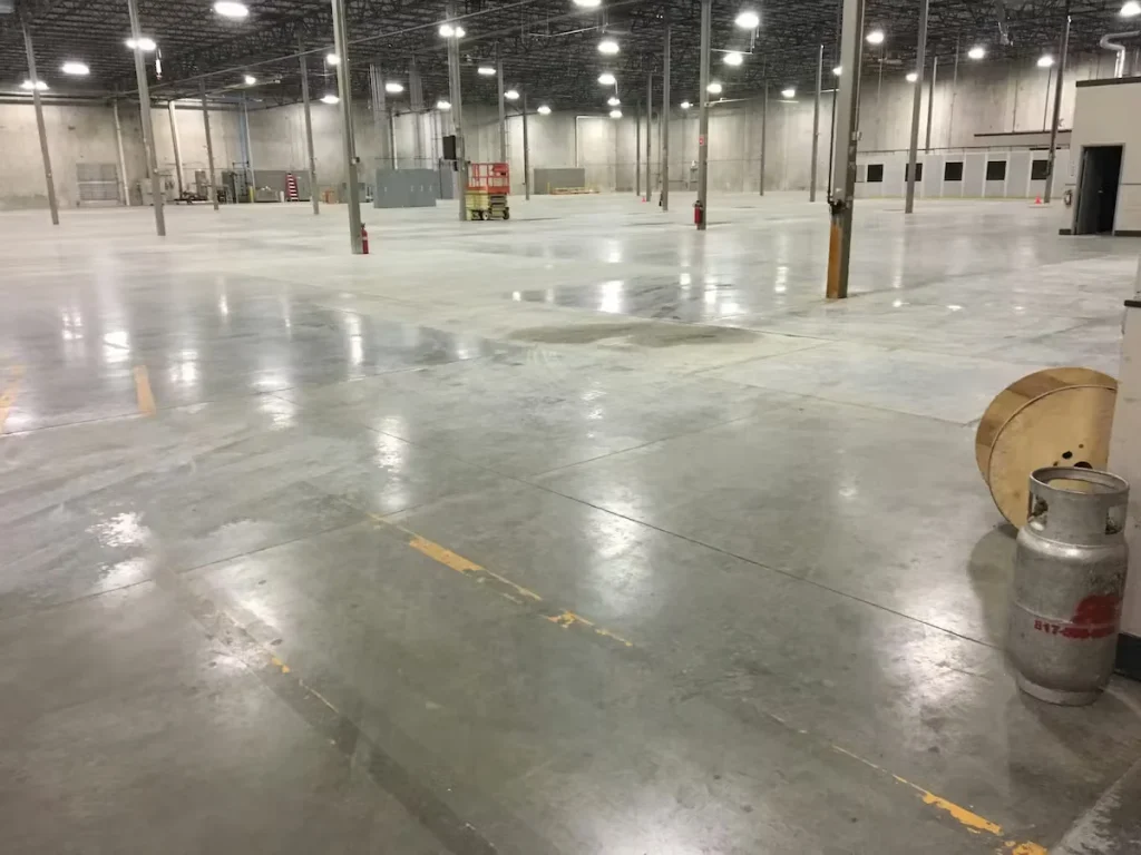 Wide warehouse interior with polished concrete floor, tall support columns, and bright overhead lighting across large open space