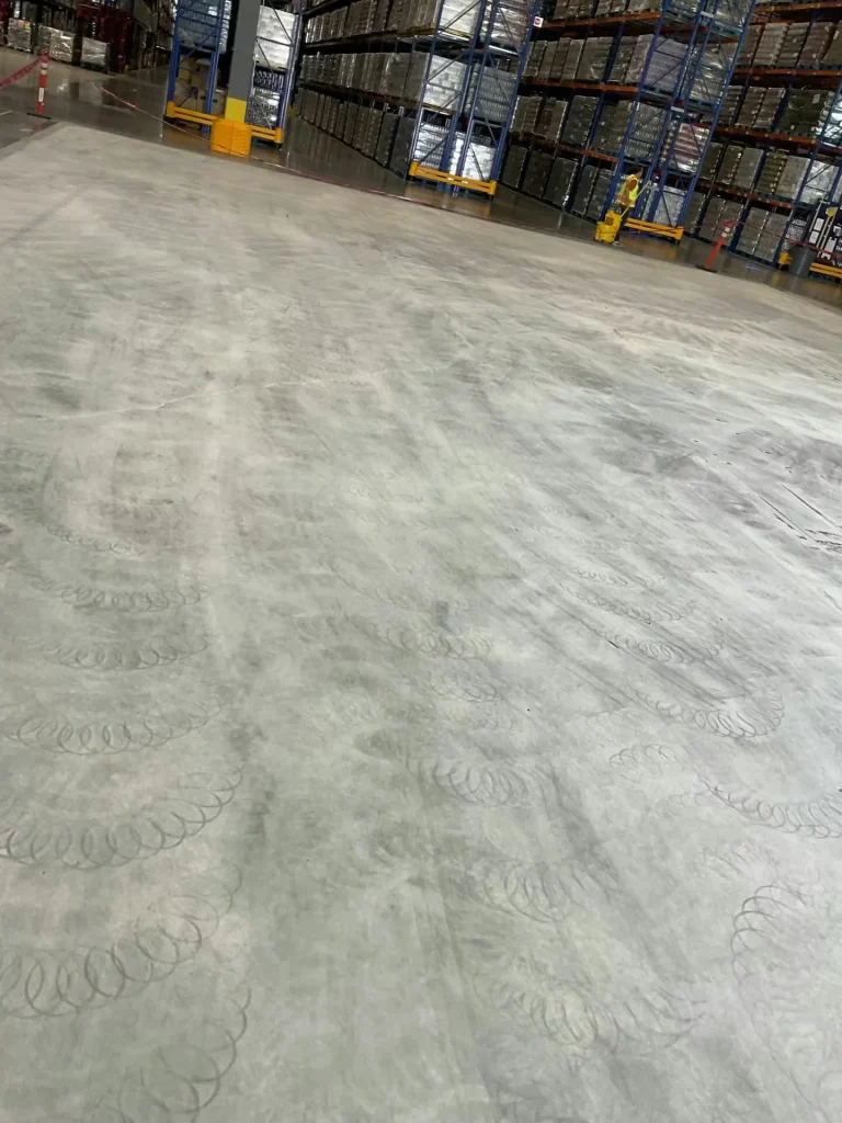 Warehouse floor being prepped and ground with visible swirl marks before coating installation