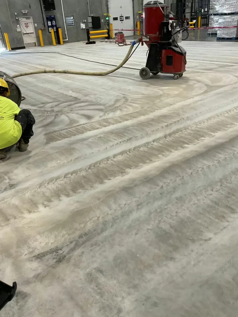 Industrial worker grinding warehouse floor with dust collection equipment during flooring installation