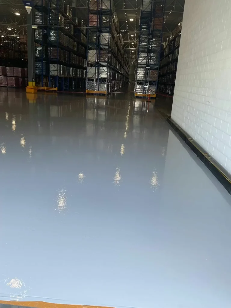 Freshly coated epoxy warehouse floor with smooth reflective finish between storage aisles