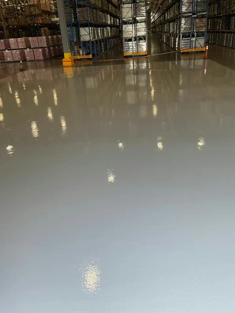 Newly installed epoxy floor in warehouse showing glossy surface and reflected overhead lighting