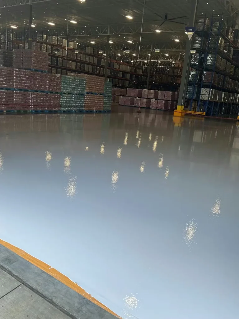 Wide view of completed epoxy warehouse flooring with pallet racks and polished gray finish