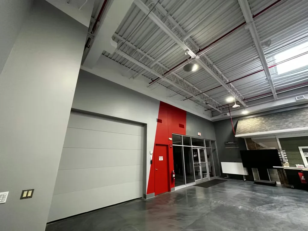 Modern warehouse interior with exposed ceiling, red accent wall, and glass entry doors
