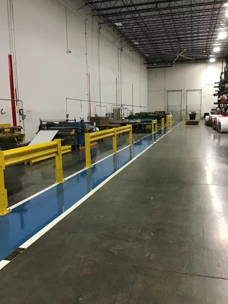 Manufacturing floor with blue painted pedestrian walkway and yellow safety guardrails separating equipment areas