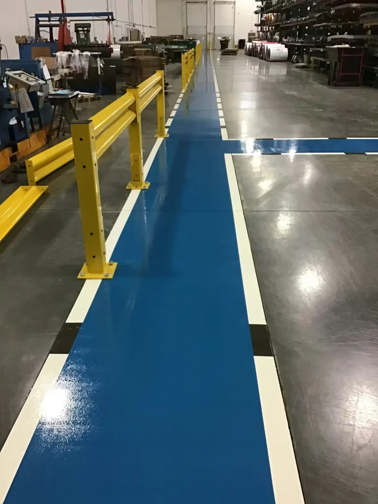 Close-up of blue floor striping marking a designated walkway inside an industrial facility with safety railings