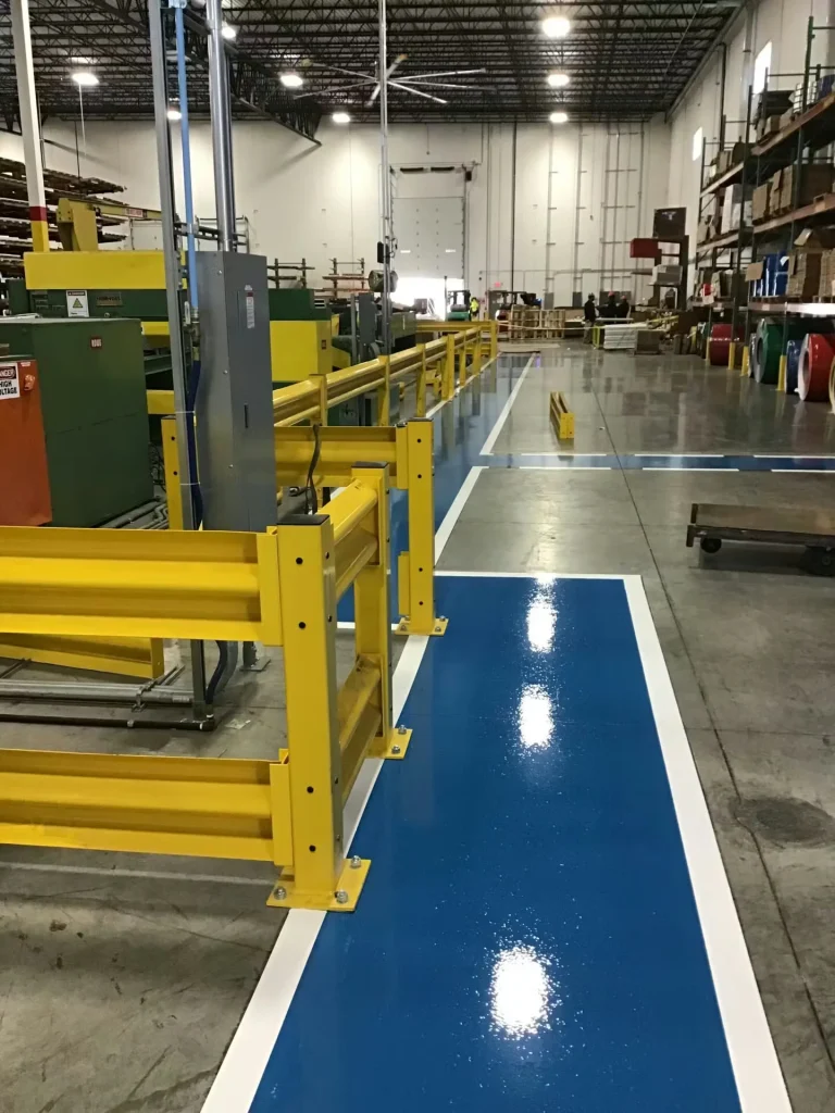 Factory interior showing newly painted blue floor lanes, yellow machine guards, and organized production areas