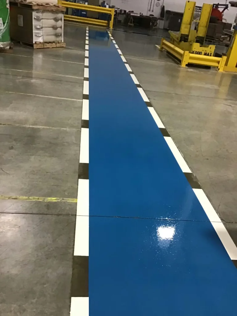 Straight blue epoxy floor walkway with white border lines guiding foot traffic through an industrial workspace