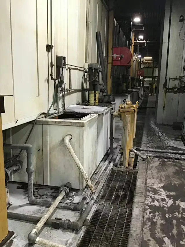 Industrial facility interior with large chemical tanks, exposed pipes, and a grated floor during maintenance cleaning