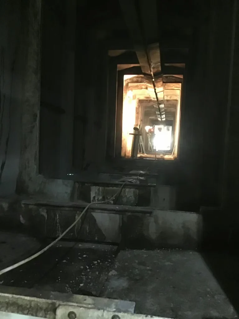 Long concrete tunnel inside an industrial plant with cables on the floor and bright light visible at the far end