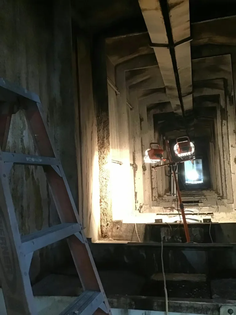 Concrete industrial shaft with temporary work lights and a ladder set up for inspection or cleaning work